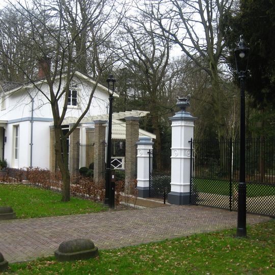 Voormalige diensthuis van de Pauw, gepleisterd. Ernaast hek met hardstenen pijlers door vazen bekroond toegang Pauwhof