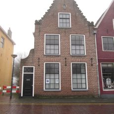 Pand tegen herbouwde klokgevel met siertrossen op de deklijsten onder zadeldak schoorsteen met bord