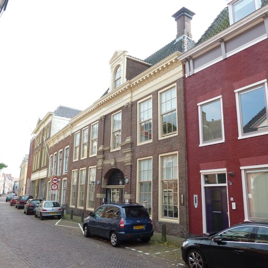 Zes traveeën breed pand met hoge geblokte kroonlijst, dakkapel en gevel met onderdelen uit de 17e eeuw