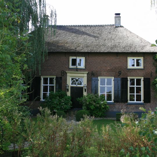 Boerderij op het T-vormige plattegrond, waarvan het woonhuis met een riet gedekt schilddak, een eenvoudige deuromlijsting en vensters met luiken en zesruitsschuiframen bezit