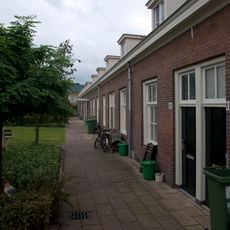 Gedeeltelijk dubbele- en gedeeltelijk enkele rij van in totaal achttien woningen op rechthoekige plattegrond, bestaande uit een bouwlaag onder een met pannen gedekt mansardedak