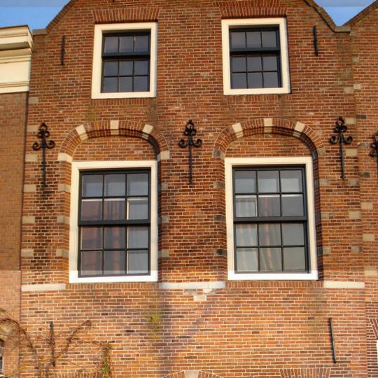 Pand met puntgevel, waarin geprofileerde en getoogde vensteromlijstingen en een topsieranker. In de sluitsteen van de inrijpoort met jaartal