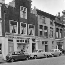 Fraaie gevel met verhoogd middenstuk, gebeeldhouwde zijstukken, gebogen fronton bekroning, gedodekopte muren, moderne winkelpui