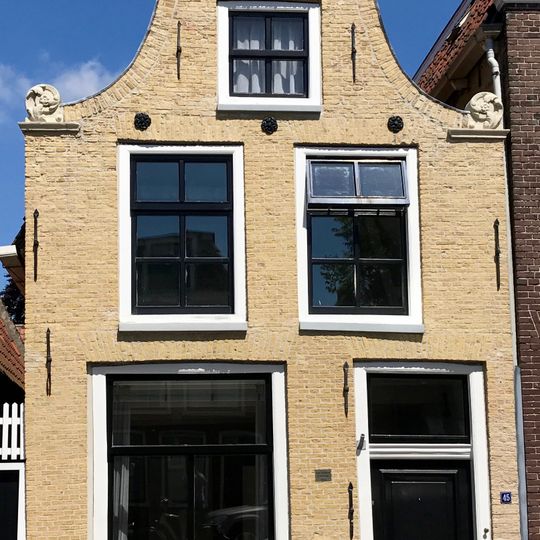 Smal pand onder zadeldak tegen ingezwenkte halsgevel met aanzetkrullen en bekronend fronton