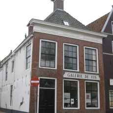 Pand met gevel met rechte kroonlijst met compartimenten onder schilddak met voorschild met twee topschoorstenen met bord