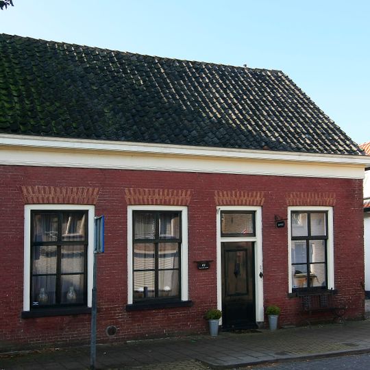 Dwarshuis van alleen begane-grond met zadeldak tussen puntgevels. Rood gesausd metselwerk met gele vensterstrekken