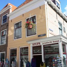 Huis met gepleisterde lijstgevel. Dakkapel. Piron. Zijgevel met uitbouw oorspronkelijk pothuis, aan de zijde van de Lepelstraat. Winkelpui