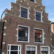 Pand met hoogoprijzende trapgevel versierd met hoek-, neg- en boogblokken rond de verdiepte vensternissen