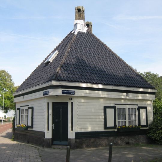 Houten gebouw met plattegrond van twee in elkaar geschoven vierkanten, voormalige politiepost, oorspronkelijk met ingang aan voorkant, bouwstijl Amsterdamse School
