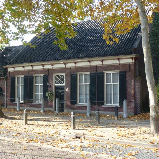 Pand bestaande uit begane-grond met hoog, pannen zadeldak tussen puntgevels met rollagen. Deur met panelen in de voorgevel; vensters met luiken en schuiframen.