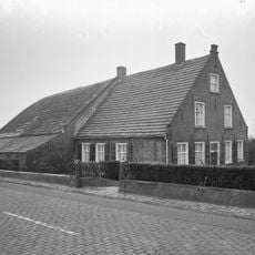 Boerderij van het Langstraatse type, met aan de voorzijde een tuitgevel, bekroond door trappen en een toppilaster. Zesdelige schuiframen en luiken. De stal met afgewolfd rieten dak