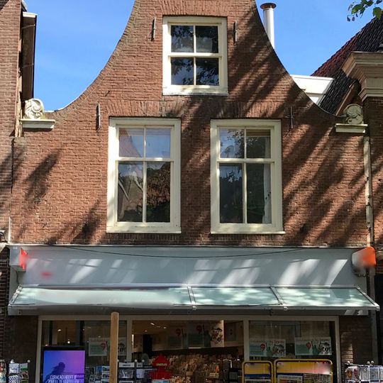 In machinale steen herbouwd lager pand met klokgevel met aanzetkrullen en gebogen deklijst