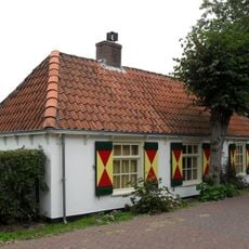 Gepleisterd pand zonder verdieping onder hoog met pannen gedekt schilddak. Twee vensters met negenruitsschuiframen in de voorgevel