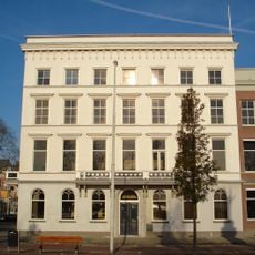 Gepleisterd hoekpand, met kroonlijst, waaronder rondboogfries, vensters met hoofdgestellen en balcons op consoles met hekken, versierd met neogotische vierpasmotieven